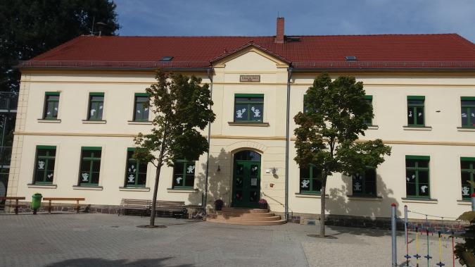 Blick auf das zweistöckige Schulgebäude, Haupteingang mit zwei Bäumen