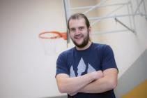 Schulleiter Herr Schmidt steht in der Turnhalle vor einem Basketballkorb und lächelt in die Kamera.